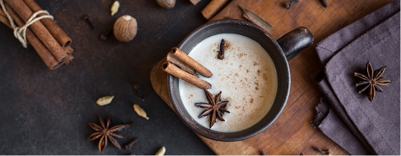 Cup of chai latte surrounded by star anise, cinnamon sticks, and other chai spices